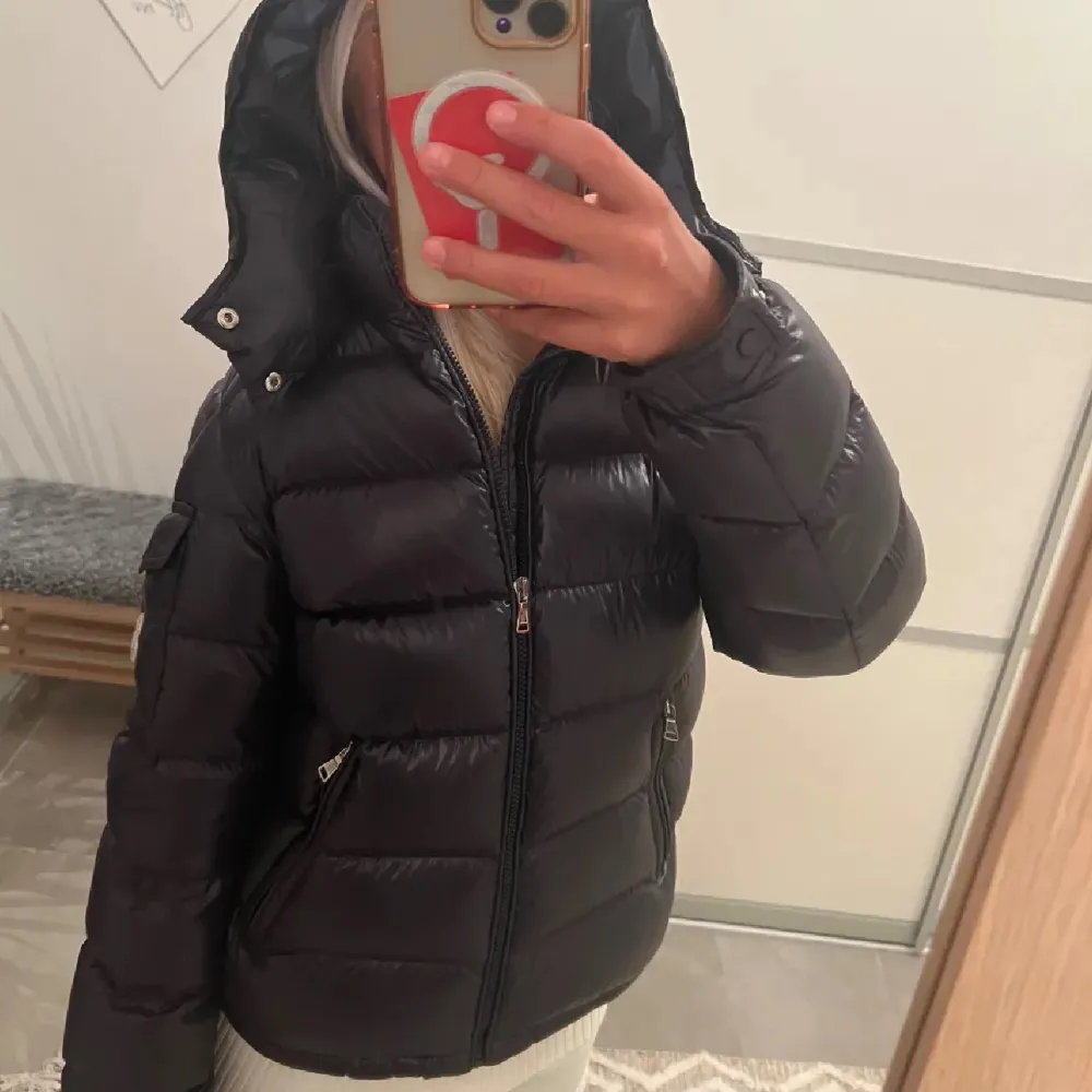 Säljer en snygg och varm svart dunjacka från Moncler some modell Maya. Jackan har en huva och dragkedja framtill, perfekt för kalla vinterdagar. Den är i mycket bra skick och har en stilren design med Moncler-loggan på ärmen. Passar perfekt för både vardag och fest!💕💋. Jackor.