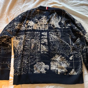 Svart mönstrad tröja från Tommy Hilfiger - Säljer en marinblå tröja från Tommy Hilfiger med ett unikt kartmönster i beige, köpt från NK i Stockholm. Tröjan har en normal passform och är långärmad, perfekt för höst och vinter. Den är i mycket bra skick och passar både till vardags och lite mer uppklädda tillfällen. Superbekväm och stilren!Står Storlek L men skulle säga att det är Medium. Hör av dig vid frågor eller funderingar!