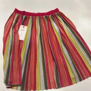 Randig glittrig kjol från kids ONLY - Superfin randig kjol från kids ONLY i glittrigt material. Den har en mix av färger som röd, gul, grön och silver, vilket gör den perfekt för att sticka ut. Kjolen har en elastisk midja för bekväm passform. Perfekt för festliga tillfällen eller när du vill lysa upp vardagen! ✨