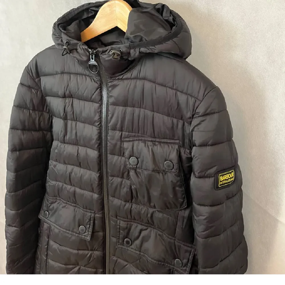 Säljer en snygg svart pufferjacka från Barbour i mycket bra skick. Jackan har en dragkedja framtill och praktiska fickor med knappar. Perfekt för höst och vinter med sin varma vaddering. Den har en huva som skyddar mot regn och vind. Passar både till vardags och lite finare tillfällen.. Jackor.