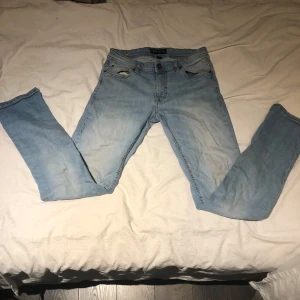 Ljusblå jeans i bra skick - Säljer ett par ljusblå jeans i bra skick. De har en klassisk femficksdesign och är tillverkade i denim. Det finns några små slitningar som ger dem en cool, använd look. Perfekta för vardagsbruk!