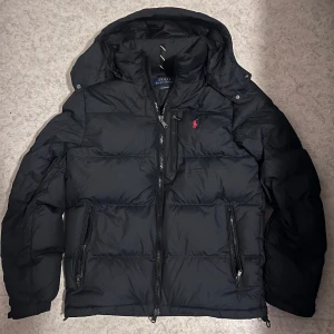 Svart/marinblå pufferjacka Polo Ralph Lauren Äkta - Säljer en snygg svart/marinblå pufferjacka från Polo Ralph Lauren Äkta i storlek S. Den är i ny skick och har en design med en liten röd logga på bröstet. Den är Perfekt för vintern!