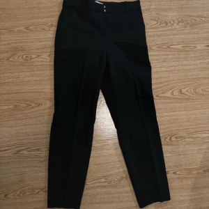 Svarta kostymbyxor - Snygga svarta kostymbyxor i klassisk stil. Perfekta för både kontoret och festliga tillfällen. De har en rak passform och är tillverkade i ett bekvämt material som ger en stilren look. Passar bra med en skjorta eller en elegant topp. Storlek 38 men mer som 36. Aldrig använda!