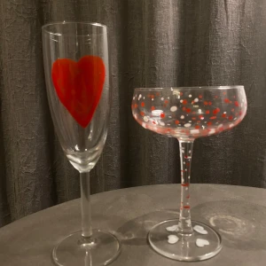 Två glas med hjärt- och prickmönster - Säljer två unika glas, ett champagneglas med ett stort rött hjärta och ett cocktailglas med röda och vita prickar. Perfekta för en romantisk kväll eller fest! Passar både till vardag och speciella tillfällen. 🥂❤️Cocktailglas 70kr, Champagneglaset 65kr