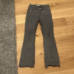 Grå byxor från Lindex - Säljer ett par grå byxor från Lindex i bra skick. De har en bootcut-stil med råa kanter längst ner. Byxorna är högmidjade och har en klassisk femficksdesign med knapp och dragkedja framtill. Perfekta för både vardag och fest!