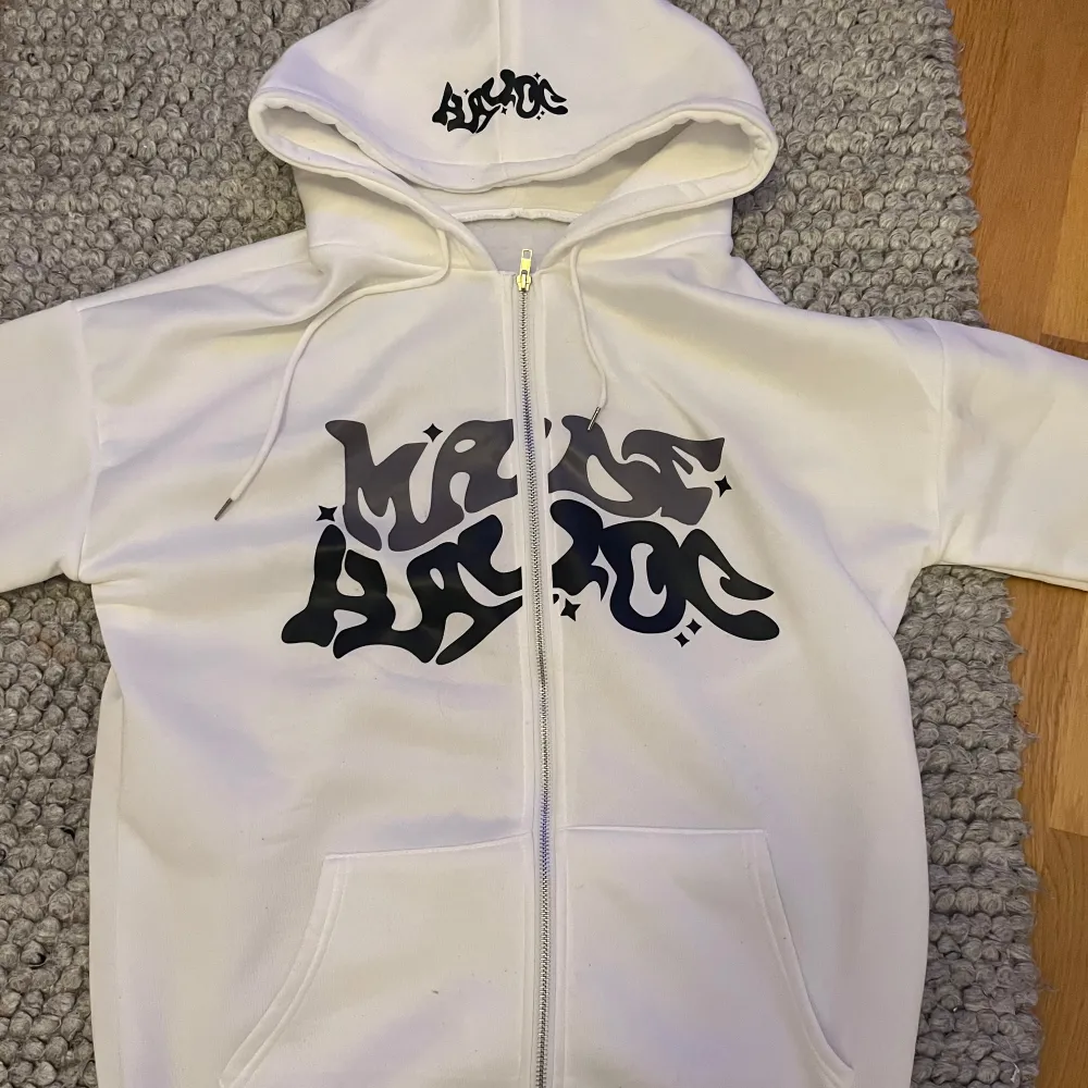 Säljer en vit hoodie med coolt svart tryck på framsidan. Den har en dragkedja och en stor luva, perfekt för att hålla sig varm och stilren. . Tröjor & Koftor.