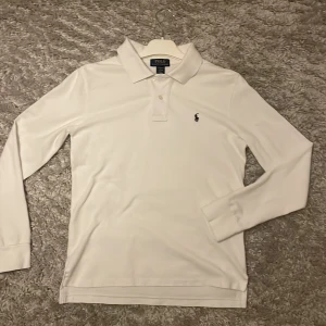 Vit långärmad pikétröja från Ralph Lauren - Säljer en klassisk vit långärmad pikétröja från Ralph Lauren. Den har en broderad logga på bröstet och är i mycket bra skick. Perfekt för både vardag och lite finare tillfällen. Mycket bra skick. Är storlek 14-16 vilket motsvarar XS.