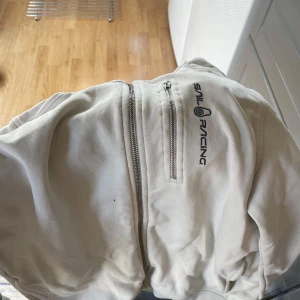 Vit tröja från Sail Racing - Säljer en vit tröja från Sail Racing i bra skick. Den har en dragkedja framtill och en liten bröstficka med dragkedja. Perfekt för vår och höst! Tröjan är stilren och passar till det mesta. Hör av dig vid intresse!