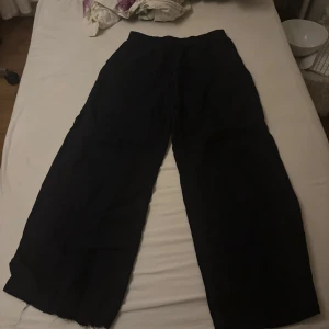 Svarta byxor med snörning - Säljer ett par svarta linne byxor i loose fit med snörning i midjan. Perfekta för en avslappnad stil och passar till både vardag och chill. De är bekväma och lätta att matcha med olika toppar. Perfekt för höst och vår! Dock väldigt korta