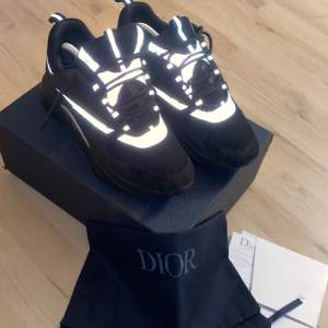 Säljer ett par svarta Dior sneakers i nytt skick. De har en cool reflekterande detalj som verkligen sticker ut. Skorna är i storlek herr 43 och kommer med originalförpackning och dustbag. Perfekta för att ge din outfit en lyxig touch!