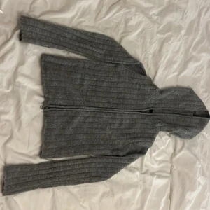 Grå stickad tröja med dragkedja från 157 - Säljer en mysig grå stickad tröja från 157 i storlek XS. Den har en dragkedja framtill och långa ärmar, perfekt för kyliga dagar. Tröjan är i bra skick och passar både höst och vinter. Perfekt för en avslappnad stil!