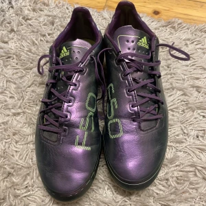 Adidas F50  - Säljer ett par coola lila Adidas fotbollsskor i ny skick har bara använt dem några gånger. De har snörning och en snygg glansig finish med vita detaljer och gröna logotyper. Perfekta för fotbollsträningen eller matchen. Skorna har en tight passform och är designade för att ge bra grepp på planen. Priset kan diskuteras!!!
