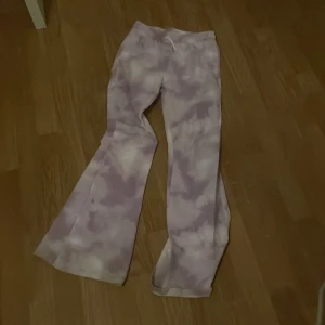 Lila batikmönstrade byxor från Kappahl - Säljer ett par supercoola lila batikmönstrade byxor från Kappahl. De har en bekväm resår i midjan och är i ett mjukt material. Perfekta för en avslappnad stil eller en chill dag hemma. Passar bra till både vardag och mysiga stunder.