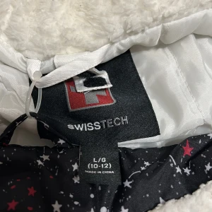 Svart och vit jacka från SwissTech - Säljer en snygg och varm jacka från SwissTech i svart och vitt. Jackan har en mysig vit fleecefoder och ett coolt stjärnmönster på insidan. Perfekt för kalla vinterdagar med dragkedja och praktiska fickor. Passar både för vardag och utomhusaktiviteter!