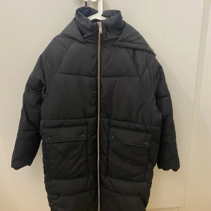 Svart pufferjacka från ONLY - Säljer en svart pufferjacka från ONLY i storlek S. Jackan har en dragkedja framtill och stora fickor med knappar. Perfekt för kalla dagar med sin varma och quiltade design. Den har en skön huva och är i mycket bra skick. Perfekt för vintern! Oversize i modellen, använde bara några gånger