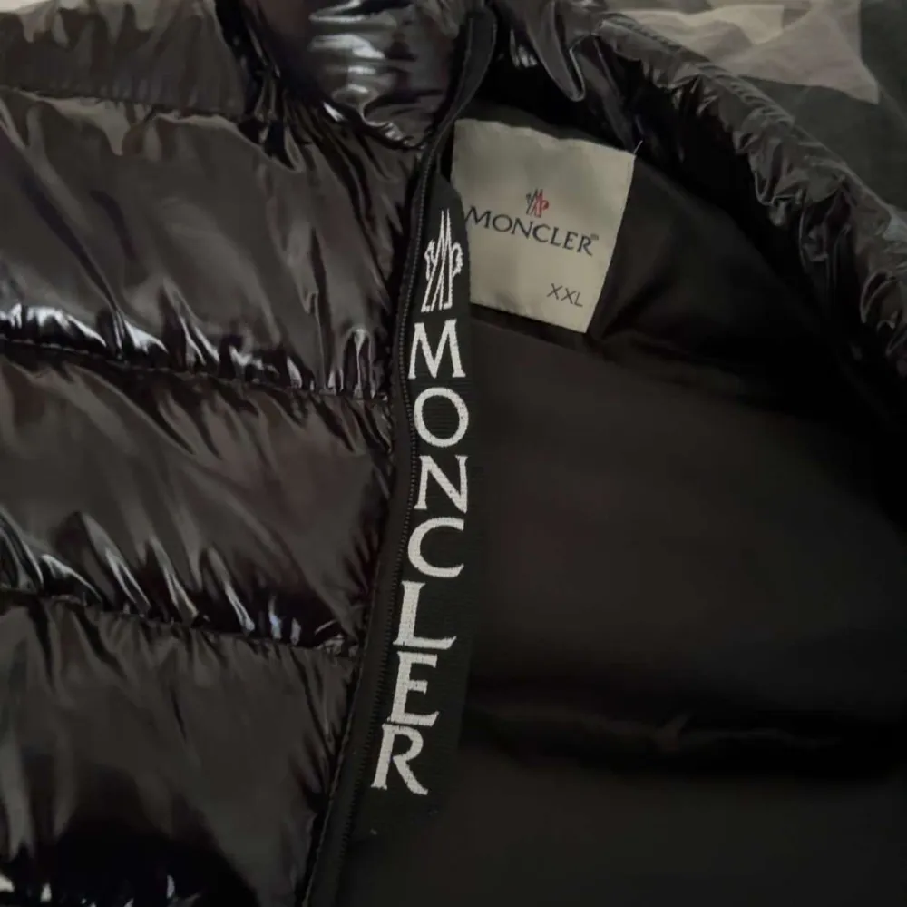 Säljer en snygg svart dunväst från Moncler det står XXL men det är XL/L. Västen har en glansig finish och dragkedja framtill. Perfekt för kyliga dagar när du vill hålla stilen. Den har också en cool serietidningsdetalj på insidan. Passar både till vardags och lite finare tillfällen.. Jackor.