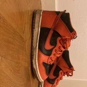 Säljer ett par coola Nike Dunk i orange och svart. Skorna har en klassisk design med snörning och är i bra skick. Perfekta för både vardag och fest! 🧡🖤