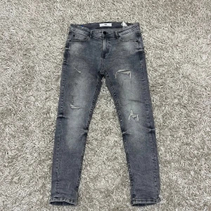 Grå jeans med slitningar - Säljer ett par grå jeans i bra skick med coola slitningar. De har en tight passform och är perfekta för en avslappnad stil. Jeansen har klassisk femficksdesign och dragkedja. Perfekta för både vardag och fest!