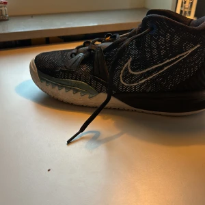 Kyrie 7 gs black and white off  - Säljer ett par svarta Nike sneakers i bra skick. De har en vit sula med ett coolt mönster och en tydlig Nike-logga på sidan. Skorna har snörning och är perfekta för träning eller vardagsbruk. Storleken är inte specificerad, men de ser ut att passa en normal passform.