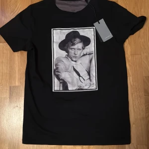 Svart t-shirt med tryck - Snygg svart t-shirt från Limitatio med ett coolt tryck av en person i hatt. Perfekt för en avslappnad stil och passar till både jeans och shorts. T-shirten är i nytt skick och har en normal passform. Ett måste för garderoben!