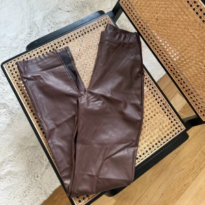 Bruna skinnbyxor - Snygga bruna skinnbyxor med en tight passform. Perfekta för att ge en edgy touch till din outfit. Byxorna har en elastisk midja för extra komfort och snygg slitsdetalj nertill 