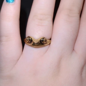 Guldfärgad ring med unik design - Säljer en guldfärgad ring med en unik och konstnärlig design. Ringen har två upphöjda detaljer som ger den ett distinkt utseende. Perfekt för dig som vill ha något annorlunda och stilfullt.