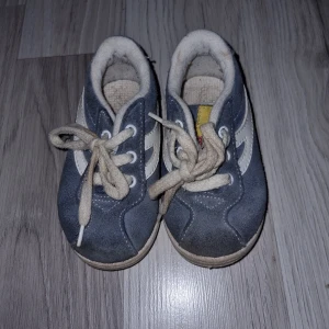 Blå barnskor med snörning - Säljer ett par blå barnskor med vita detaljer och snörning. Skorna har en robust sula och är tillverkade i mocka. Perfekta för små äventyrare!
