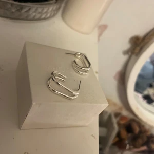 Silvriga örhängen i modern design - Snygga silvriga örhängen med en modern och stilren design. De har en unik form som ger en trendig look. Perfekta för att komplettera din outfit med en touch av elegans.