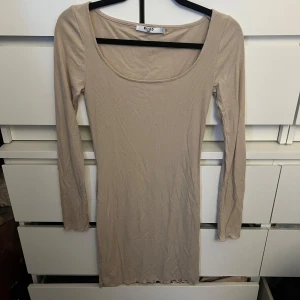 Beige ribbad klänning från NA-KD - Säljer en stilren beige ribbad klänning från NA-KD. Klänningen har en tight passform och långa ärmar, perfekt för en chic look. Den är tillverkad i ett mjukt och bekvämt material som formar sig fint efter kroppen.