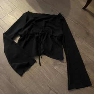 Svart långärmad topp med knyt - Snygg svart topp med långa ärmar och knytning framtill. Perfekt för en stilren look. Materialet är mjukt och bekvämt.