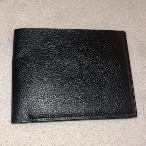 Svart plånbok i skinn - Snygg och stilren svart plånbok i skinn med flera kortfack och en genomskinlig ficka för ID eller foto. Perfekt för att hålla ordning på dina kort och kontanter. Enkel och klassisk design som passar alla tillfällen.