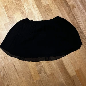 Svart kortkjol - Snygg svart kortkjol med en luftig design. Perfekt för att matcha med olika toppar och accessoarer. Kjolen har en enkel och stilren look som passar till många tillfällen.