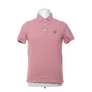 Rosa pikétröja från Lyle & Scott - Säljer en snygg rosa pikétröja från Lyle & Scott. Tröjan har en klassisk krage med tre knappar och ett broderat emblem på bröstet. Tillverkad i 100% bomull för en skön och luftig känsla. Perfekt för en avslappnad stil.