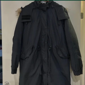 Svart parkajacka från Monki oversizes  - Säljer en svart parkajacka från Monki med quiltad insida och pälskantad huva. Jackan har dragkedja och knappar framtill samt praktiska fickor. Perfekt för kyliga dagar! 