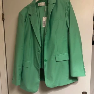 Grön kavaj - Snygg grön kavaj med klassisk design och knappar framtill. Perfekt för att ge en färgklick till din outfit. Kavajen har långa ärmar och fickor framtill. Det finns även byxor till som medföljer om man väljer att köpa 