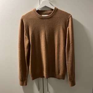 Brun merinoulltröja från These Glory Days - Säljer en stilren brun tröja i superior merinoull från These Glory Days. Tröjan har en klassisk rund hals och långa ärmar med ribbade muddar. Skick 9/10 använd nån gång bara 
