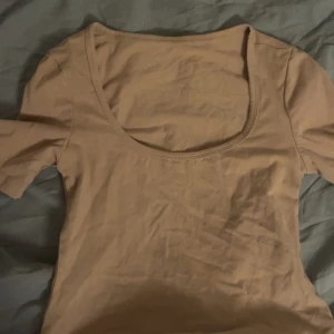 Beige kortärmad topp - Säljer en stilren beige topp. Den har korta ärmar och en rund halsringning, perfekt för en avslappnad look. Tillverkad i ett mjukt och bekvämt material.