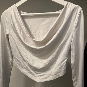 Vit långärmad topp - Säljer en stilren vit långärmad topp med draperad framsida. Perfekt för en elegant och avslappnad look. Toppen är croppad och har en mjuk och bekväm passform.