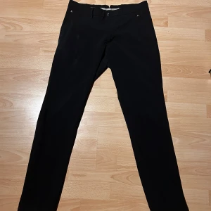 Svarta golfbyxor från J.Lindeberg - Snygga svarta golfbyxor från J.Lindeberg i tight fit. Perfekta för en stilren look med dragkedja och knapp framtill. Tillverkade i ett bekvämt material som passar bra till olika tillfällen. Aldrig använda eftersom jag fick dem och de var för små.