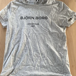 Grå t-shirt från Björn Borg - Snygg grå t-shirt från Björn Borg med tryck 'Stockholm 1956' på framsidan. Perfekt för en avslappnad stil. Tillverkad i mjukt material för extra komfort.