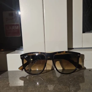 Rayban Boyfriend - Snygga solglasögon från Ray-Ban med en klassisk Wayfarer-design. Bågarna har en mörk färg med ett subtilt mönster som påminner om sköldpaddsskal. Perfekta för soliga dagar och ger en cool stil. Har lite repor och är använda.