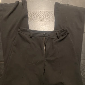 Svarta kostymbyxor - Snygga svarta kostymbyxor med dragkedja och knapp framtill. De har en klassisk design med vida ben och hällor för bälte. Perfekta för en stilren look.