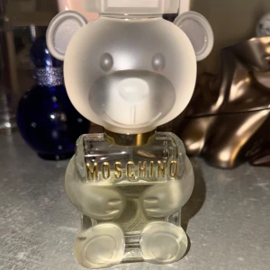 Moschino TOY2 EDP - Unik parfymflaska från Moschino formad som en björn. Flaskan är genomskinlig med frostad yta och har guldfärgad text. Perfekt för den som älskar lekfull design och vill ha något speciellt på parfymhyllan. Ca 22 ml kvar.