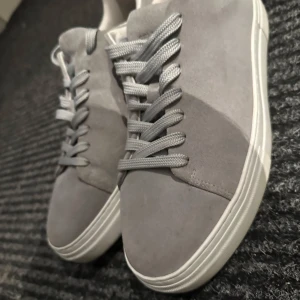Grå sneakers från Selected Homme - Snygga grå sneakers i mocka från Selected Homme. Skorna har en stilren design med snörning och en vit sula som ger en modern look. Perfekta för en avslappnad stil. Nypris 1299 mitt pris 650  priset går att diskuteras. Använd vid ett fåtal tillfällen. Finns små defekter. 