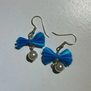 Blå örhängen med rosett och pärlor - Supersöta och charmiga örhängen med blå rosetter och vita pärlor.💙 Perfekta för att ge en färgglad touch till din outfit.