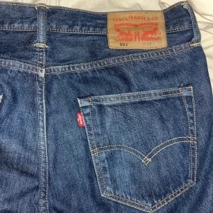Levis 501 jeans - Klassiska Levis 501 jeans i blå denim med knappgylf. De har en rak passform och är tillverkade i slitstarkt jeansmaterial. Perfekta för en tidlös stil.