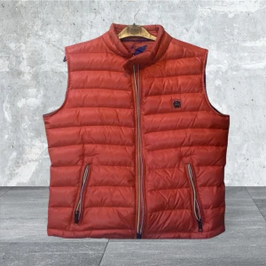 Orange dunväst från Metregó - Snygg röd dunväst från Metrego med dragkedja och två fickor framtill. Perfekt för lager-på-lager under kyliga dagar. Västen har en quiltad design och en hög krage för extra värme.