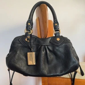 Marc jacobs väska - Så snygg Marc jacobs väska ifrån classic q kollektionen. Modellen heter babygroove. Svart med guldiga detaljer. I väldigt fint skick använd väldigt lite, nästan som ny! Måtten är ca 33x20x15cm.