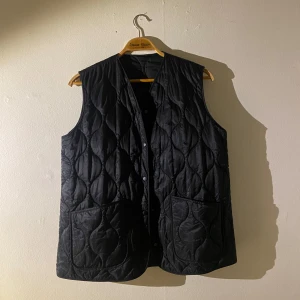 Svart väst från &otherstories - Svart quiltad väst med knappar framtill från &otherstories. Oanvänd