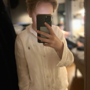 Vit linneskjorta från Polo Ralph Lauren - Säljer en stilren vit linneskjorta från Polo Ralph Lauren. Skjortan har långa ärmar och klassiska knappar framtill. Den ikoniska loggan är broderad på bröstet i blått. Perfekt för en avslappnad men ändå elegant look.